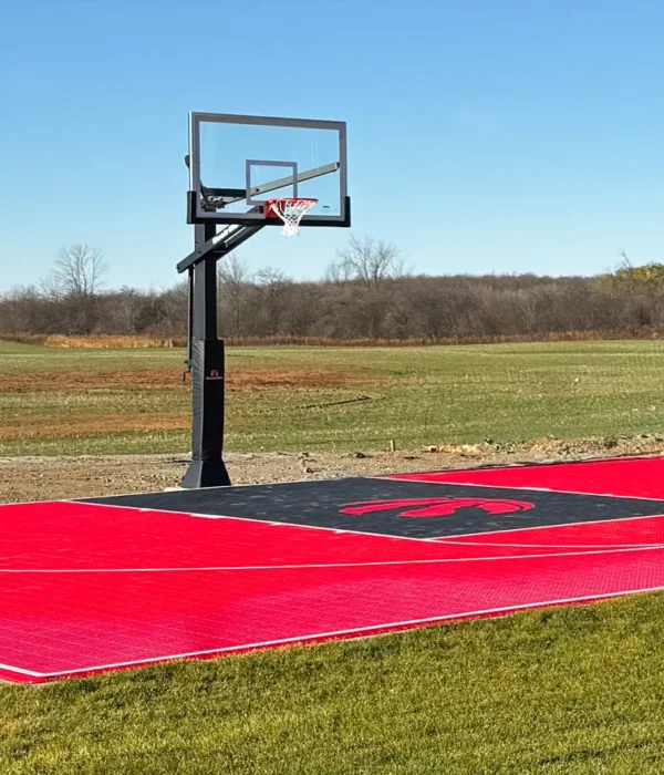 A custom design Toronto Raptors red and black backyard basketball court installed by Elite Courts next to a field