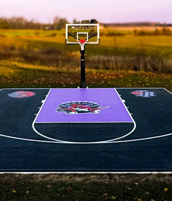 A custom design Toronto Raptors purple and black backyard basketball court installed by Elite Courts next to a field