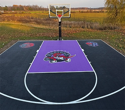 A custom design Toronto Raptors purple and black backyard basketball court installed by Elite Courts next to a field