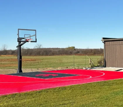 A custom design Toronto Raptors red and black backyard basketball court installed by Elite Courts next to a field