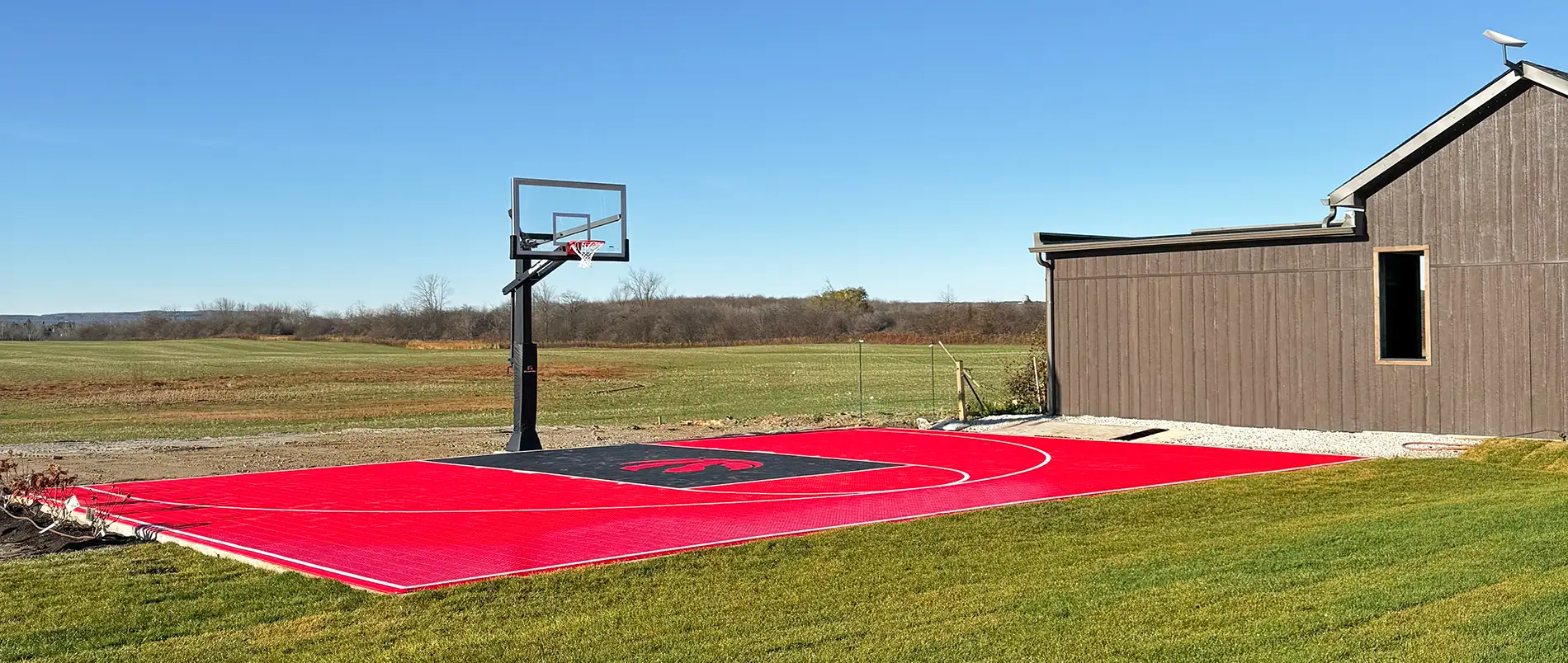 A custom design Toronto Raptors red and black backyard basketball court installed by Elite Courts next to a field