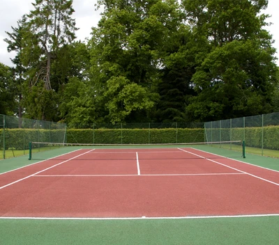 A tennis court installed in the backyard of a person's home with fencing around it