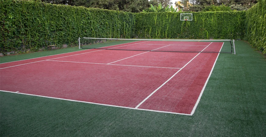 A tennis court installed with tall beautiful green bushes all around it