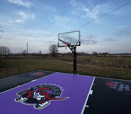 A custom design Toronto Raptors purple and black backyard basketball court installed by Elite Courts next to a field
