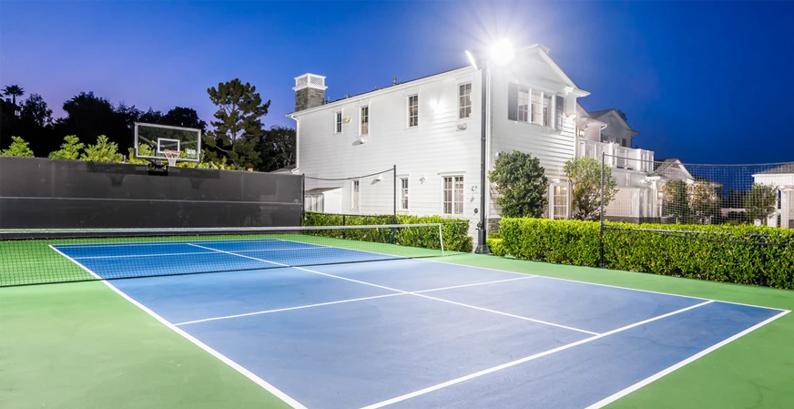 An outdoor backyard pickleball court installed with lighting